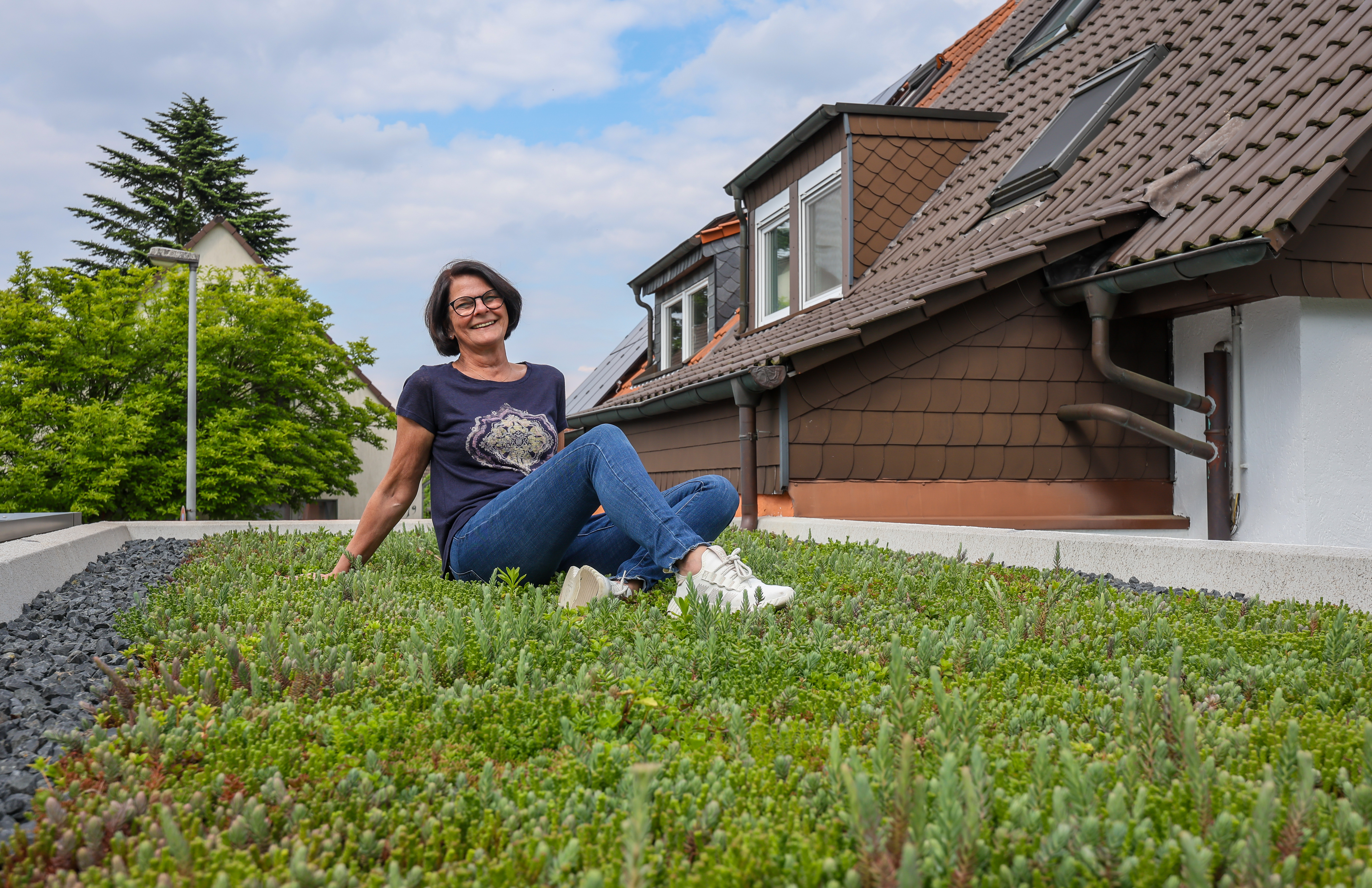 Eine Frau mit braunen Haaren und blauem Shirt sitzt auf einer begrünten Garage.