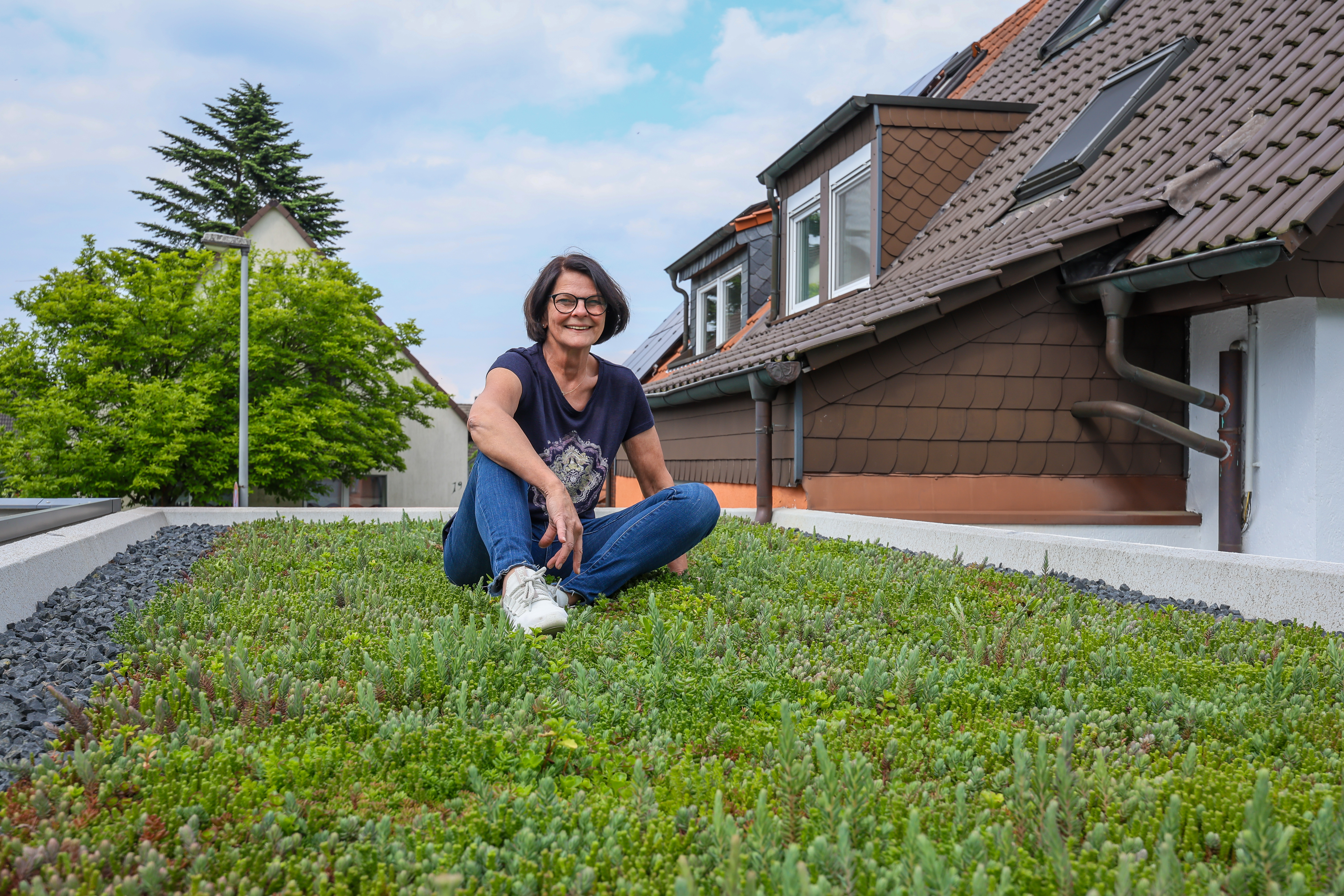 Eine Frau, Gerrit Buckesfeld, sitzt lässig mit verschränkten Beinen auf ihrem begrünten Garagendach. Im Hintergrund ist das Hausdach zusehen.
