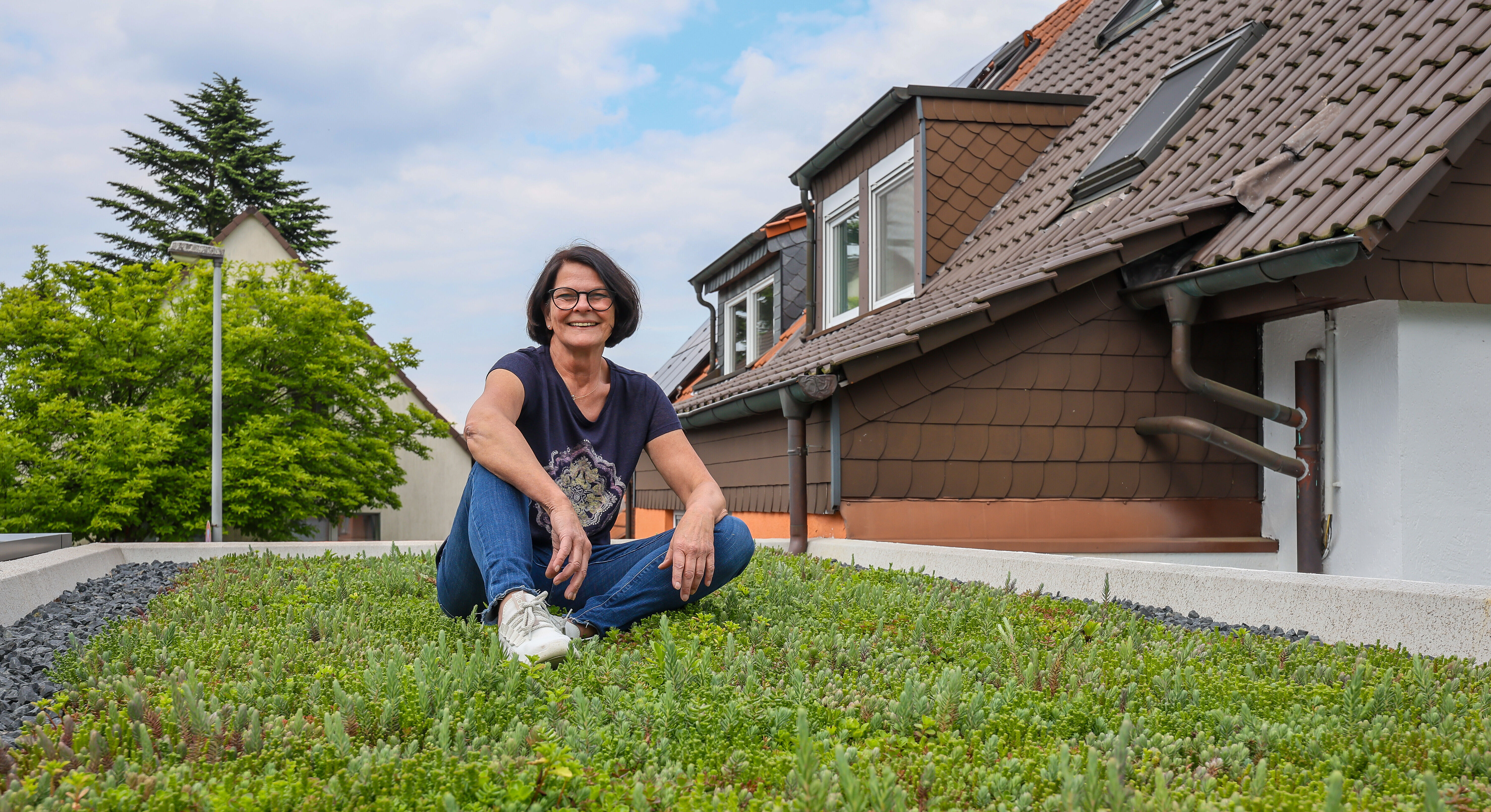 Eine Frau mit braunen Haaren und blauem Shirt sitzt auf einer begrünten Garage.